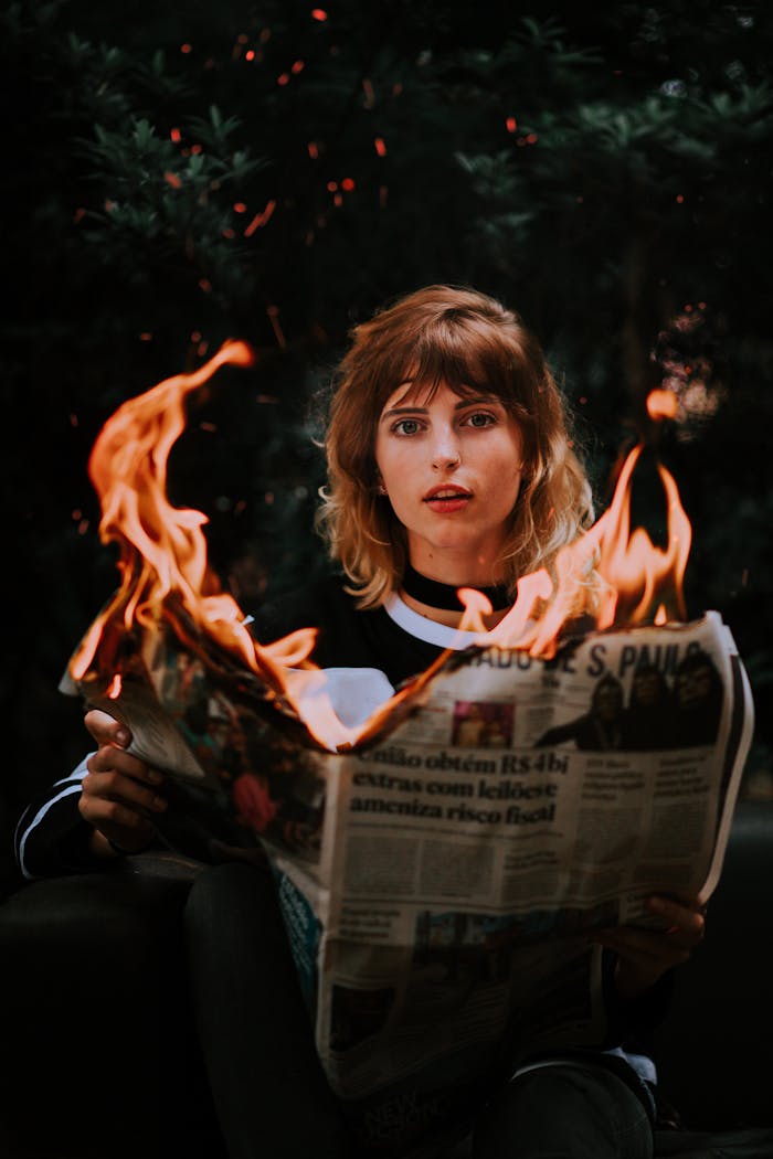A young woman holding a burning newspaper, creating a dramatic scene.